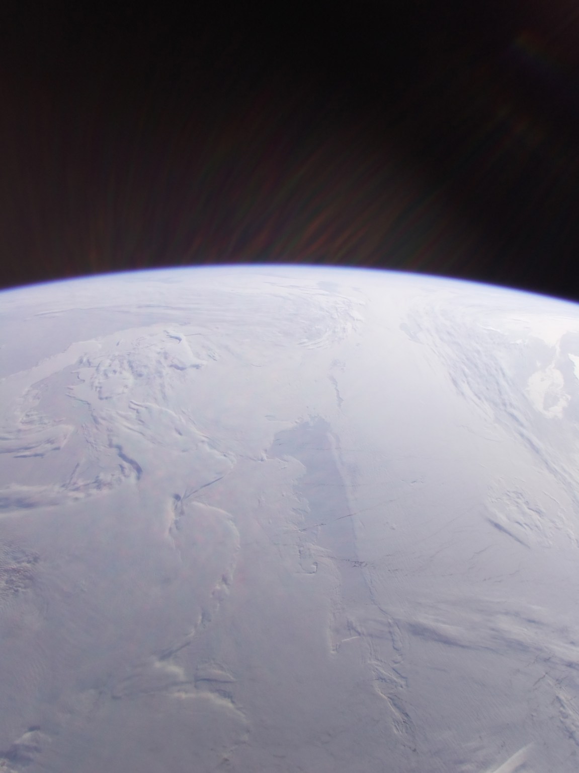 A snow-covered view of the polar cap from space. The curvature of the Earth is visible along the horizon against a dark background.