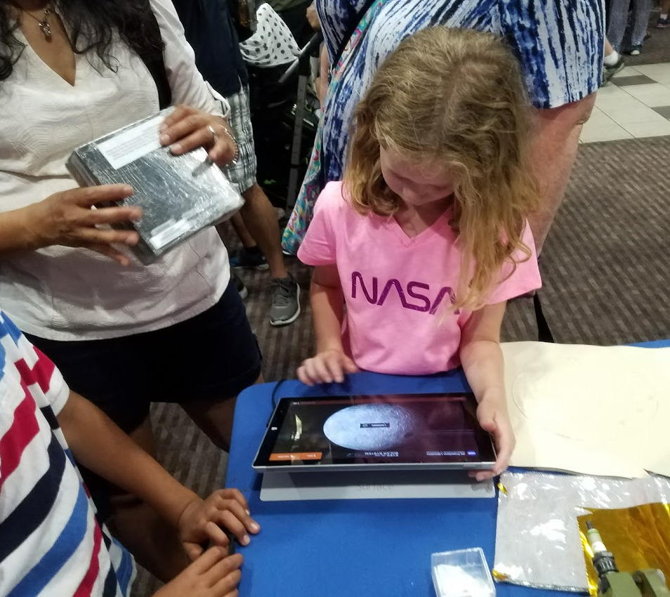 A girl in a NASA shirt explores an Eyes on the Solar System interactive kiosk at the Explore JPL event.