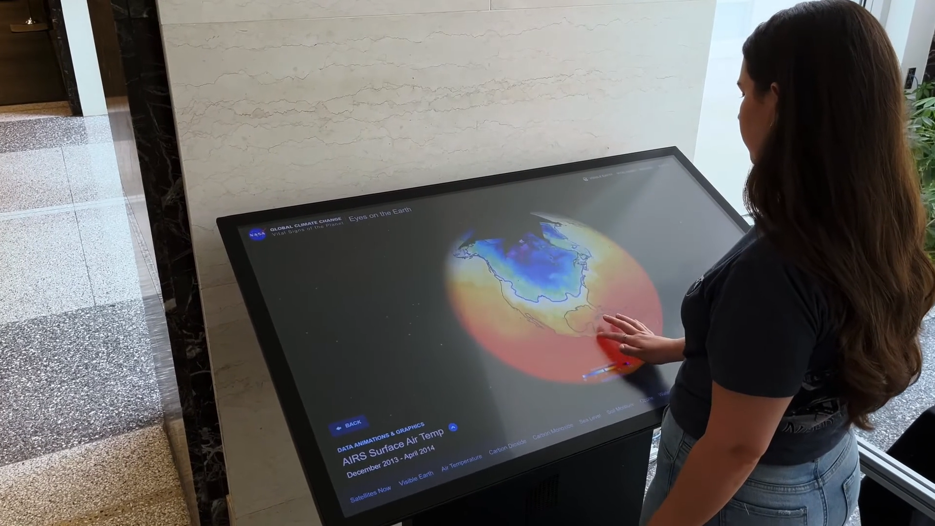 A woman interacts with an Eyes on Earth exhibit touch table.