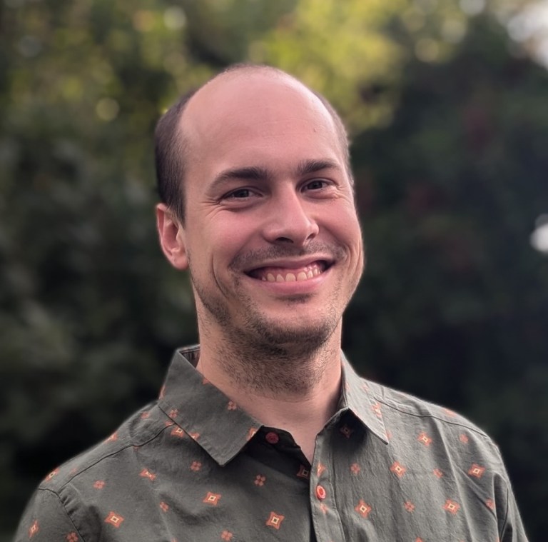 Researcher Nicholas Kruczek smiling in a button-up shirt with trees in the background.