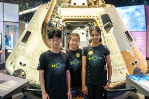 A boy and two girls standing in front of an Apollo space capsule.