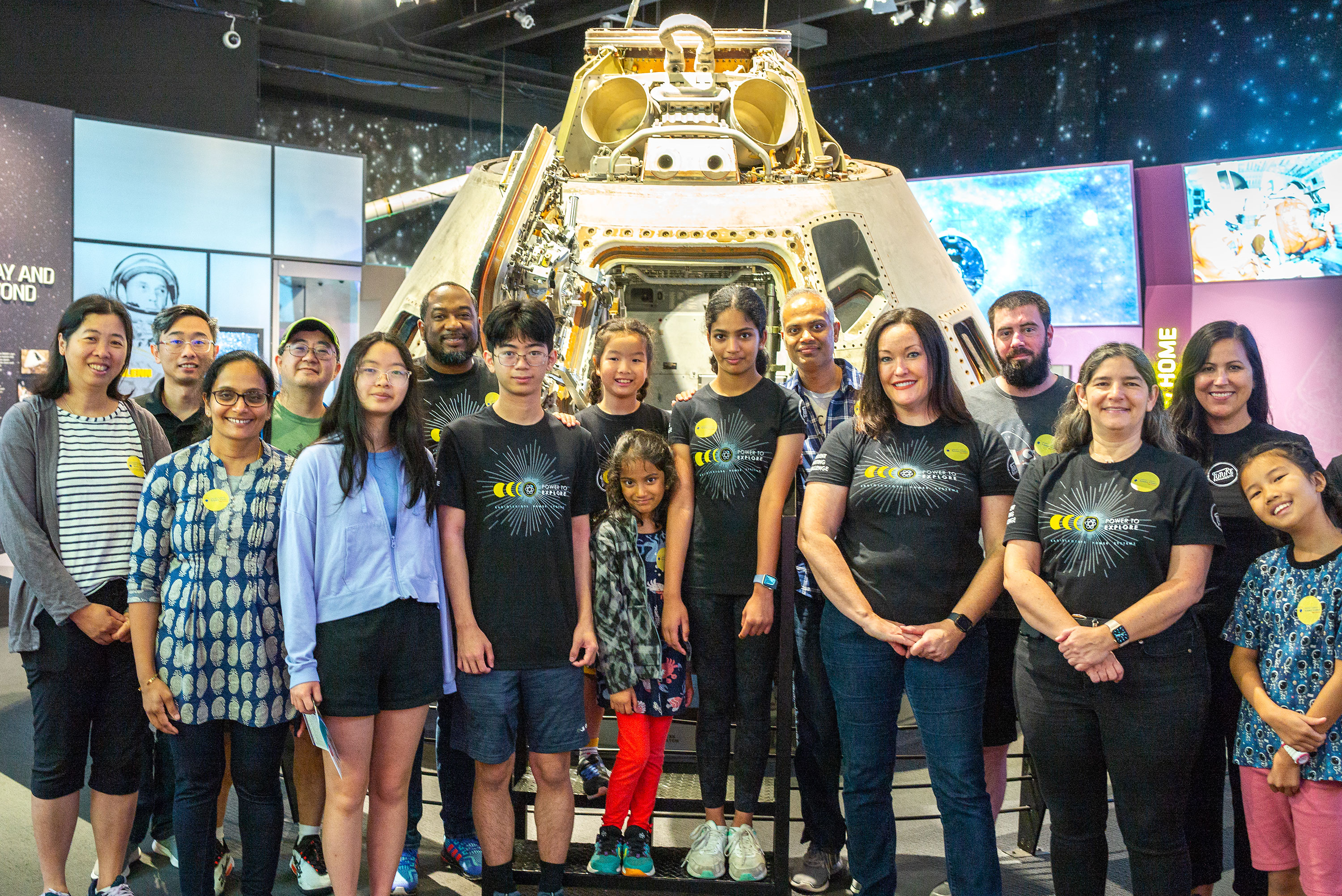 A group of men and women are standing in front of an Apollo space capsule.