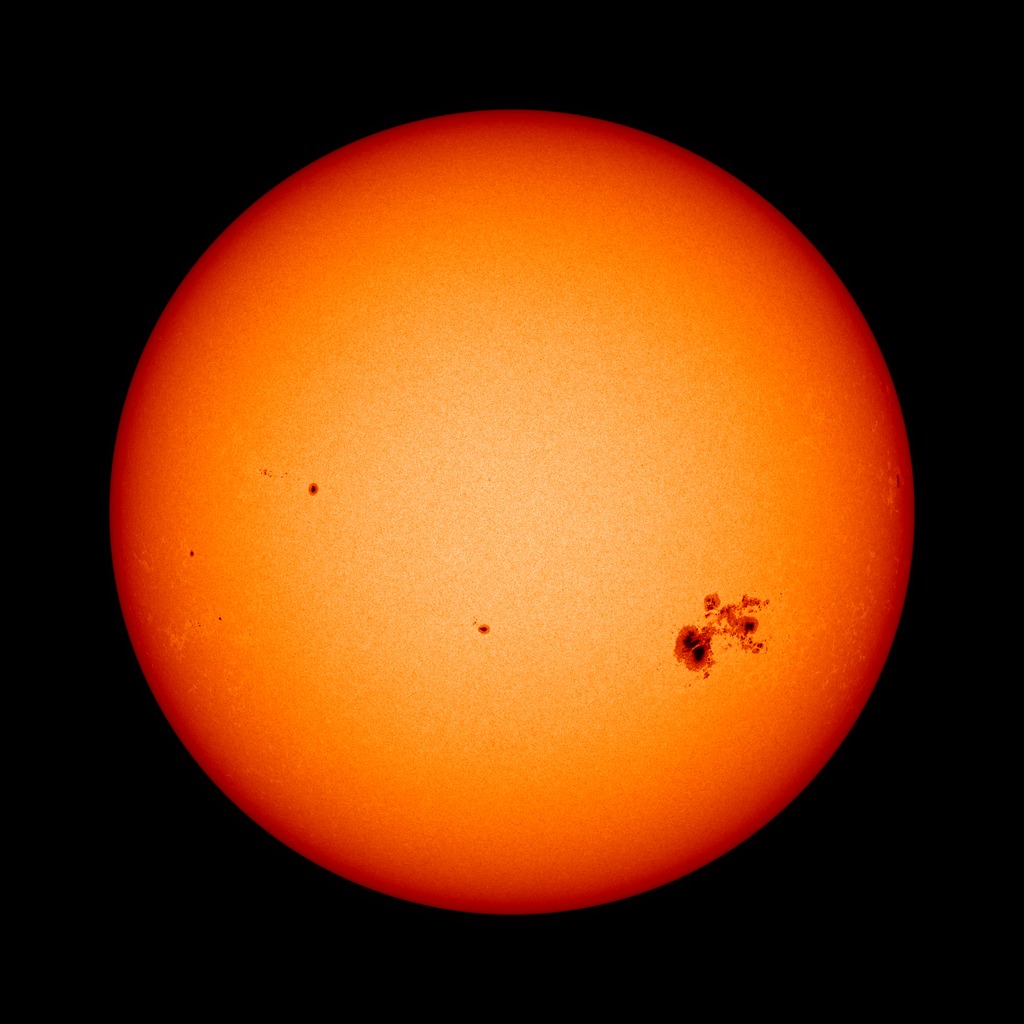 The Sun, shown against a black background. It is red toward the edges and fades to a light orange in the middle. Toward the right on the star, there is a large dark splotch — a sunspot.