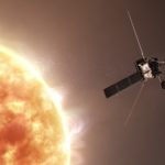 A portion of the Sun fills most of the left side of the image. On the right against the backdrop of space, Solar Orbiter, with two long panels protruding from each side of a silver box, and antenna attached to the top, back, bottom left, and bottom right, is slightly turned toward the star.