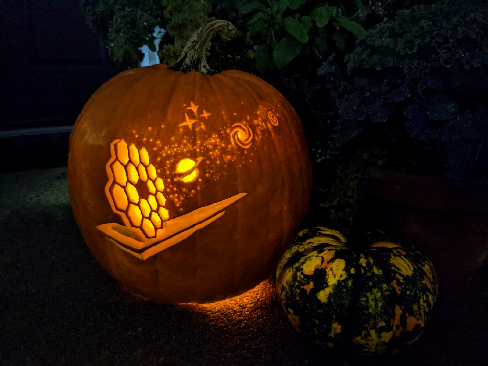 Pumpkin carving of the James Webb Space Telescope with planets, stars, and other cosmic objects; carved by Kelly Lepo.