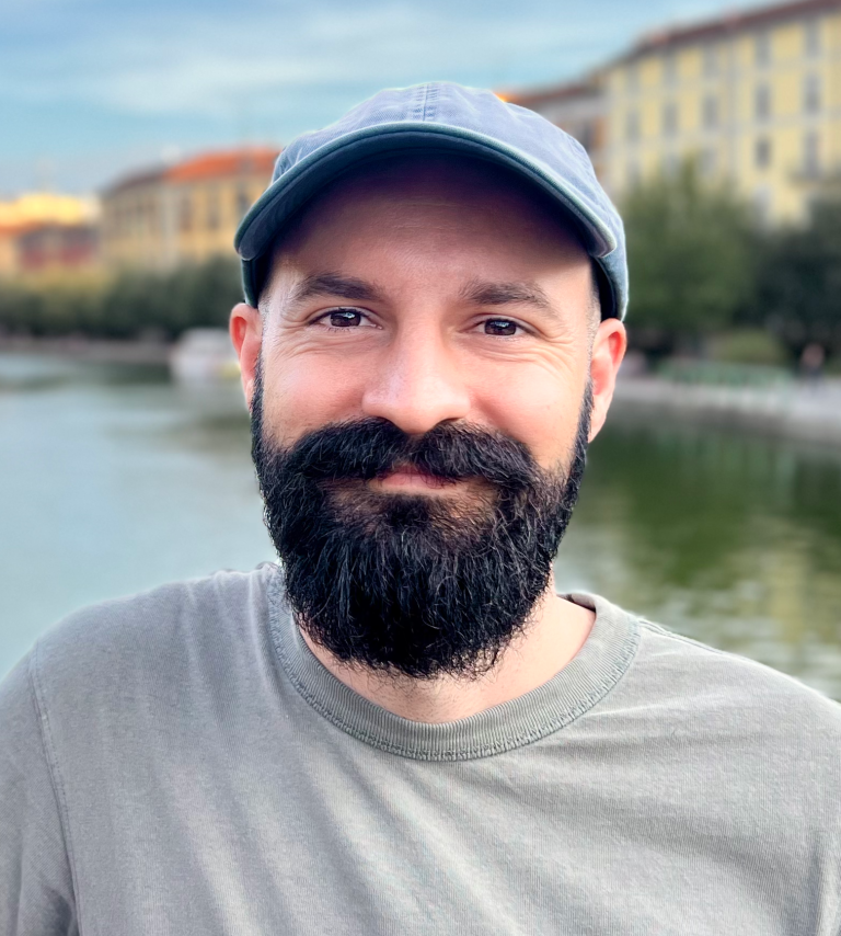 Scientist Kyle Van Gorkom smiling with a dark beard and a light blue hat in front of a canal.