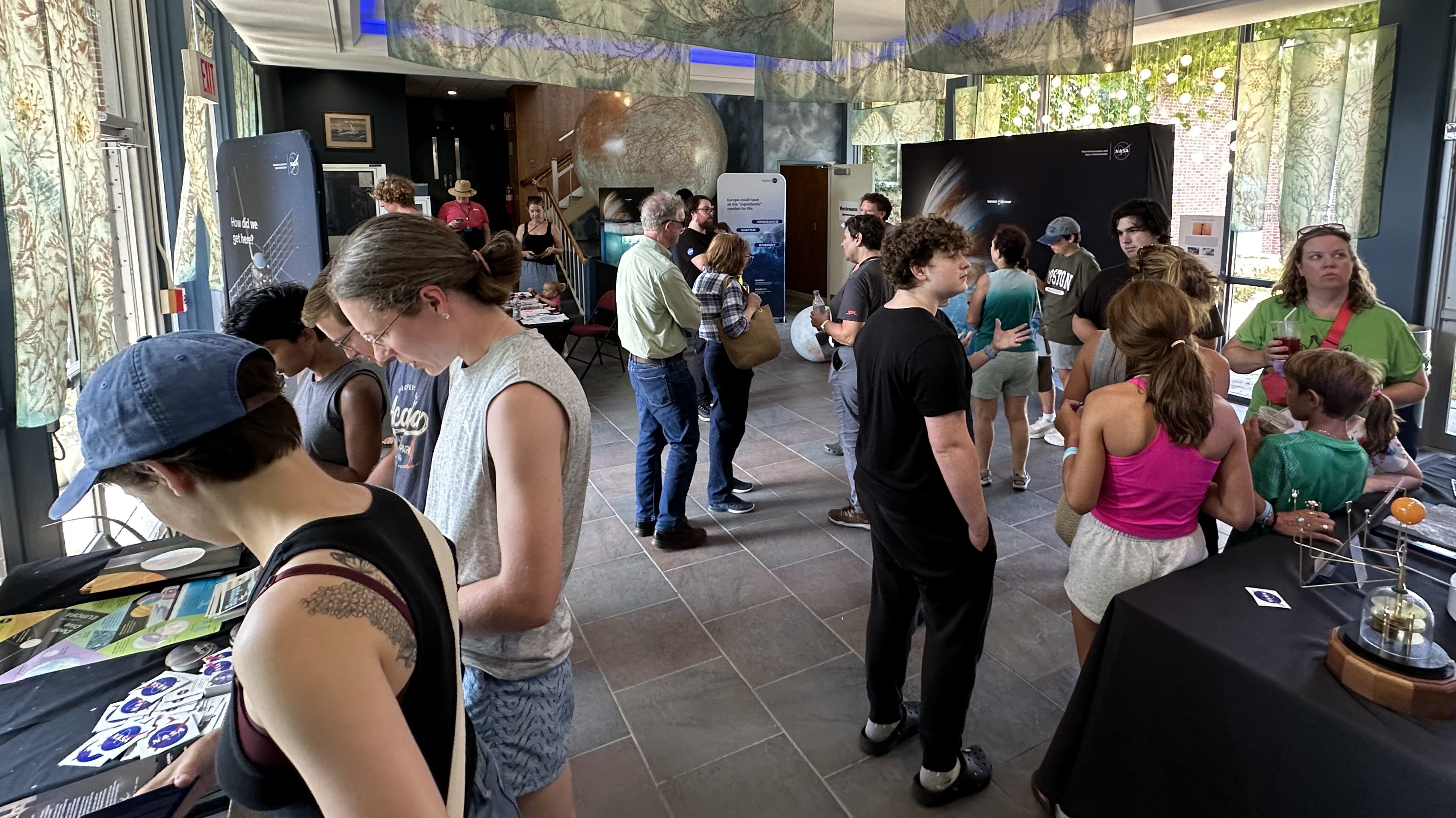 A crowd of people view exhibits and talk to NASA staff and volunteers.