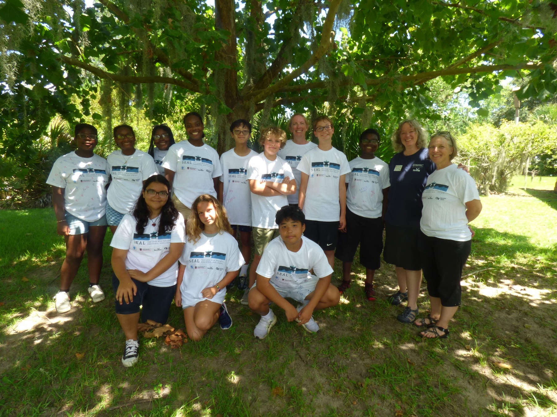 Middle school students and camp counselors standing in front of a tree smiling.