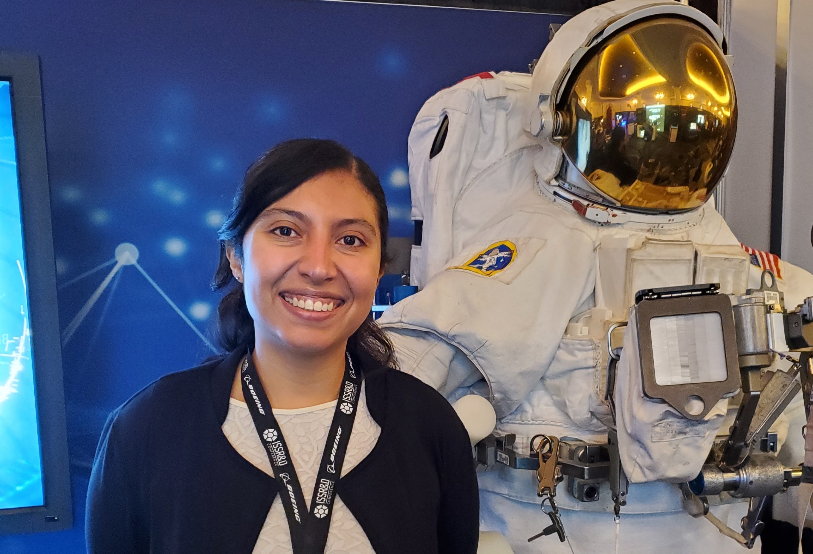 KBR employee America Reyes Wang stands next to a spacesuit display.