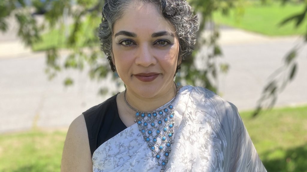 Anita Dey wearing a silver top and a necklace with blue stones.