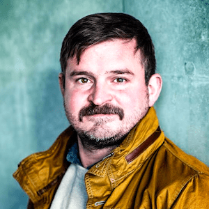 A white man with a mustache and a yellow jacket looking directly at the camera.