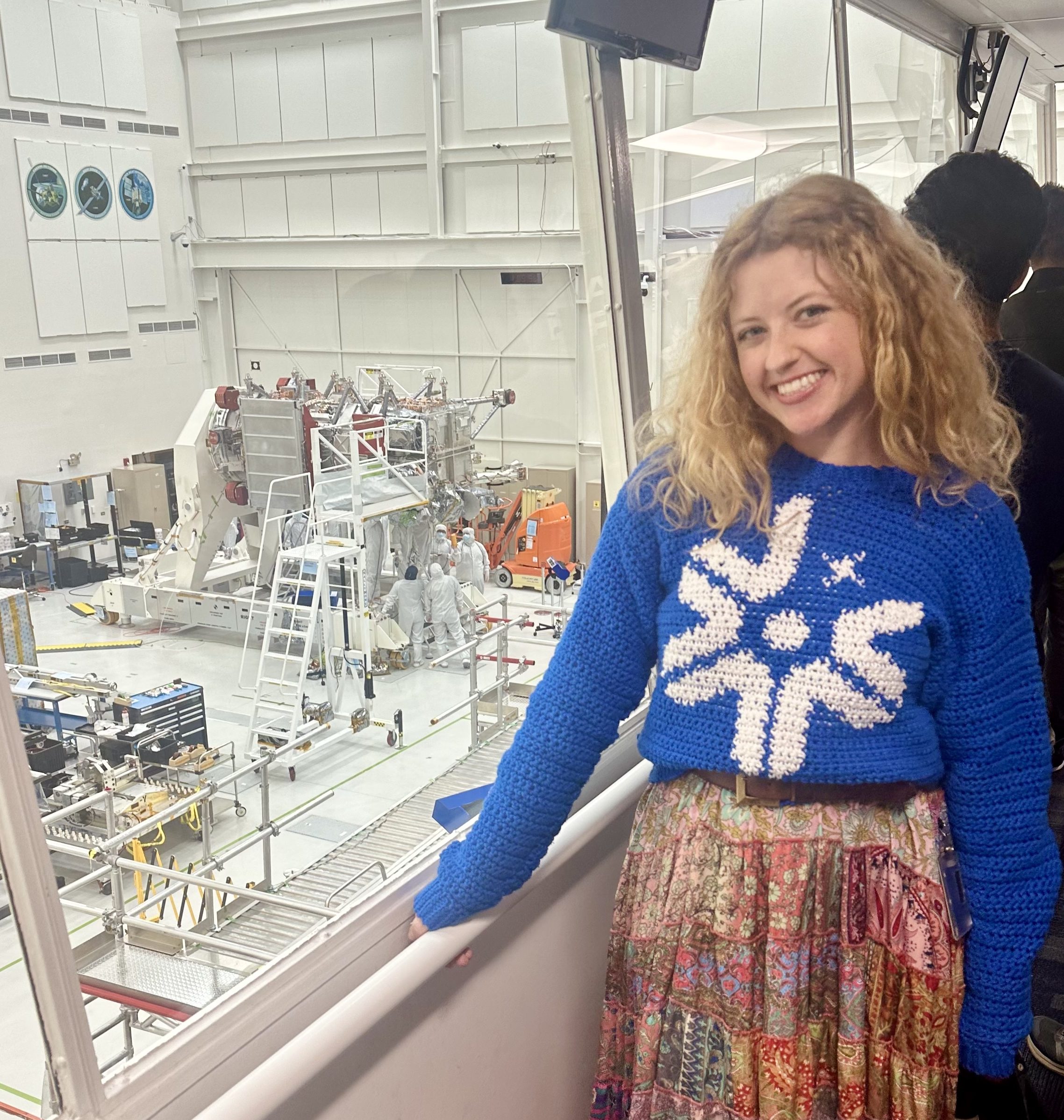 Emily Martin wears a blue sweater with the Europa Clipper logo in white as she looks out over the clean room where workers were assembling Europa Clipper.