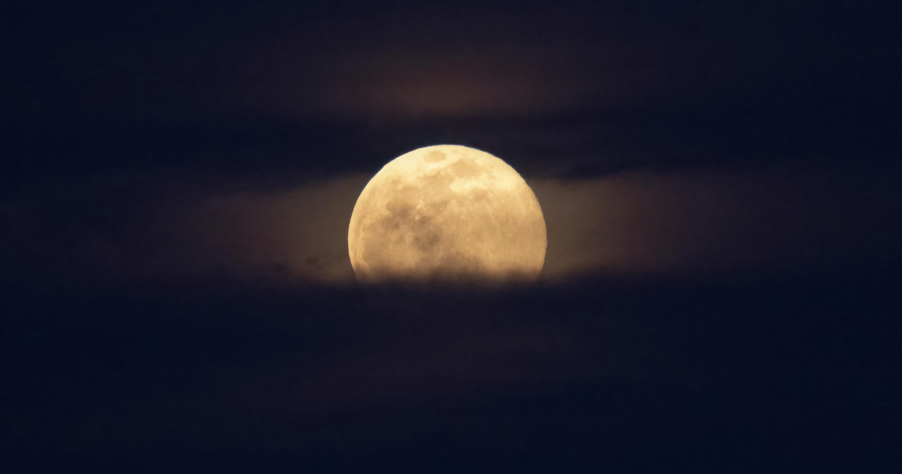 NASA News A full moon rises over a bank of clouds in the night sky.