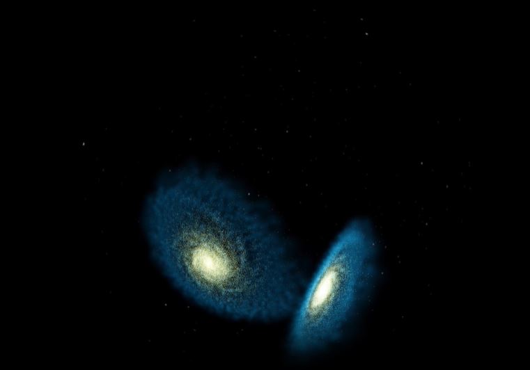 This scientific visualization holds two simulated galaxies that appear to be merging. The galaxies are set against a black background with bright yellow-white centers that extend into blue-white disks. The two galaxies are at nearly right angles to each other--one nearly face on, the other nearly edge on.