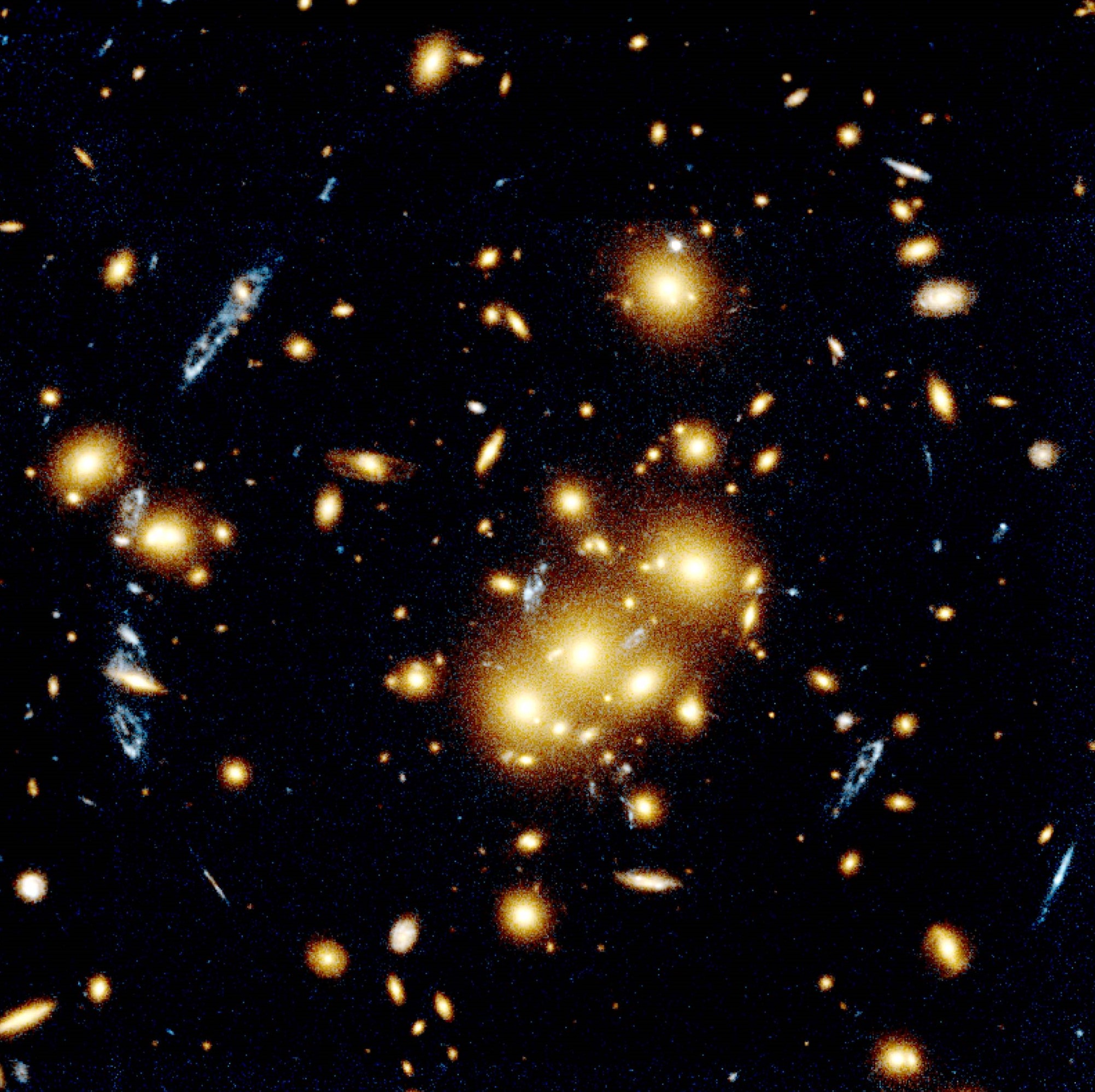 Several bright elliptical and spiral galaxies cluster near the image's center, while many others dot the field of view. Elongated, blue ellipses around the central cluster are a distant, gravitationally lensed galaxy.