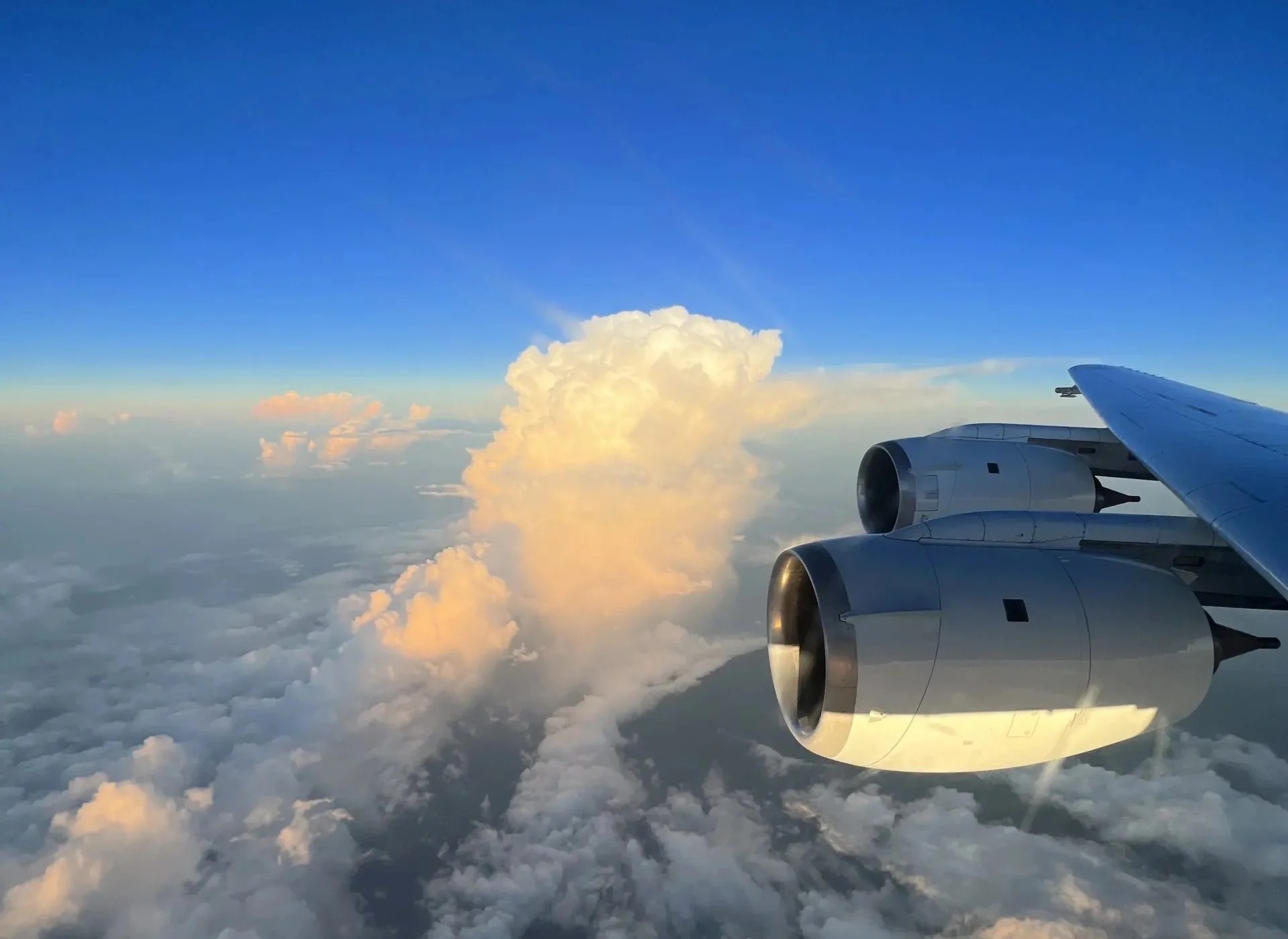 clouds below dark blue sky with plane wing and two engines