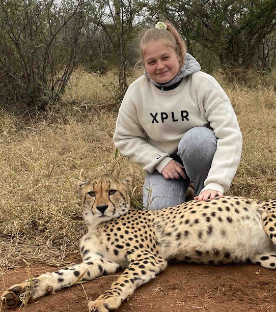 Photo of a young woman kneeling next to a large spotted wild cat