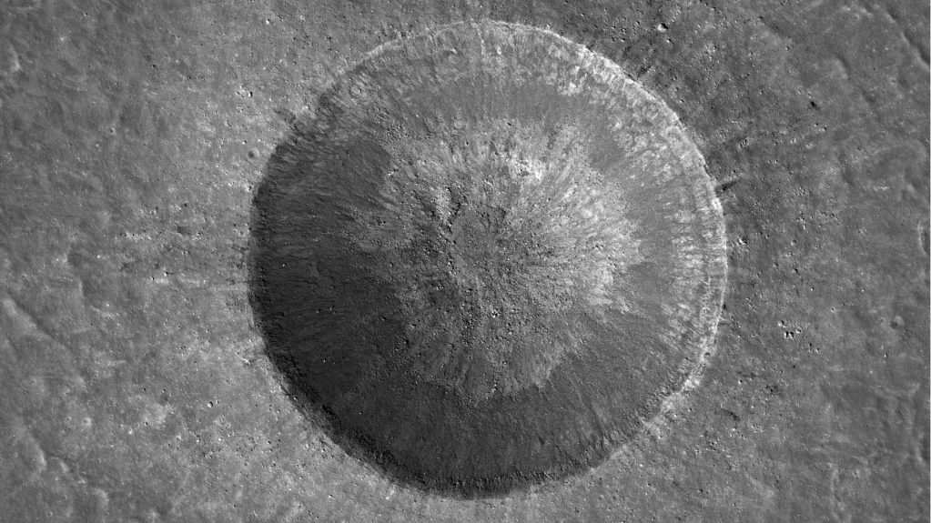 Linne Crater in shades of gray. The crater is very round with spoke-like streaks radiating away from the center along the walls of the crater. Rubble is visible in and around the crater.