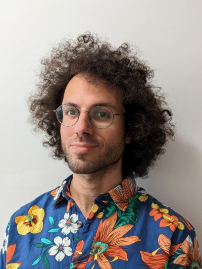 Portrait photo of a man with dark curly hair and glasses wearing a Hawaiian shirt.