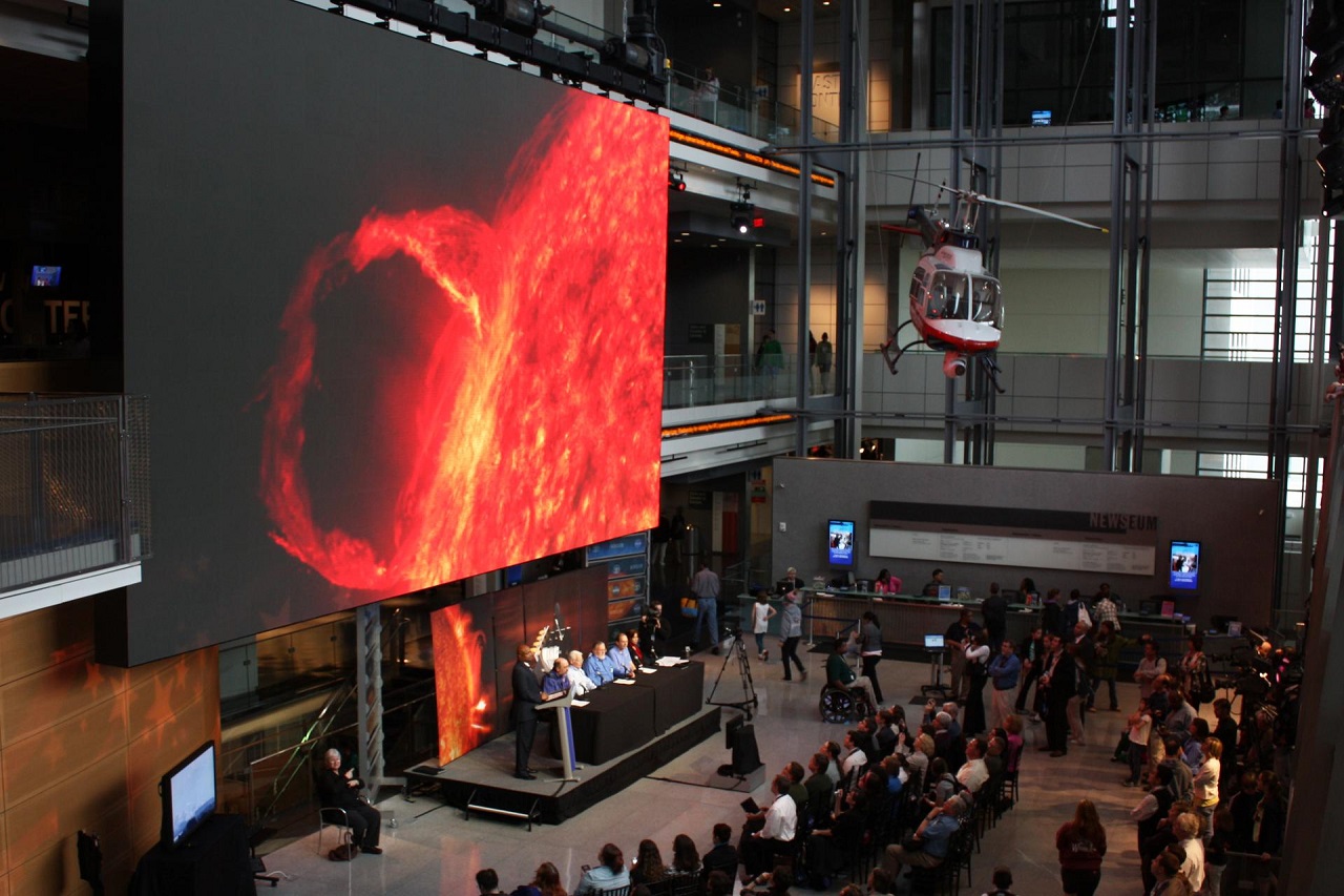 An image of a solar flare on a large display with several people in the audience.