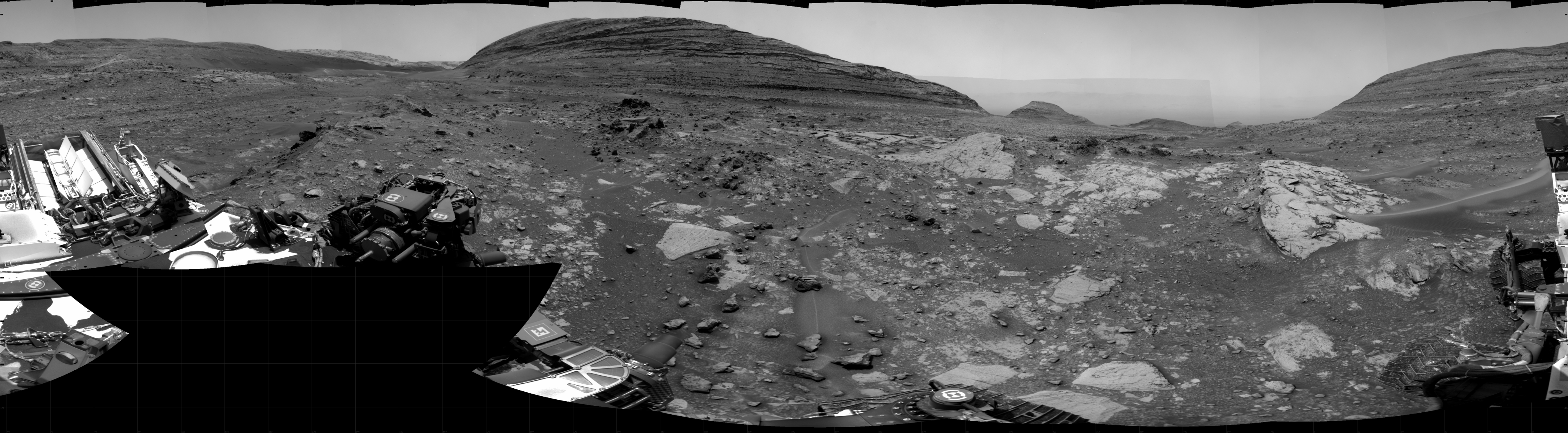 A grayscale panoramic image of the Martian surface shows booth sky and ground well-lit.