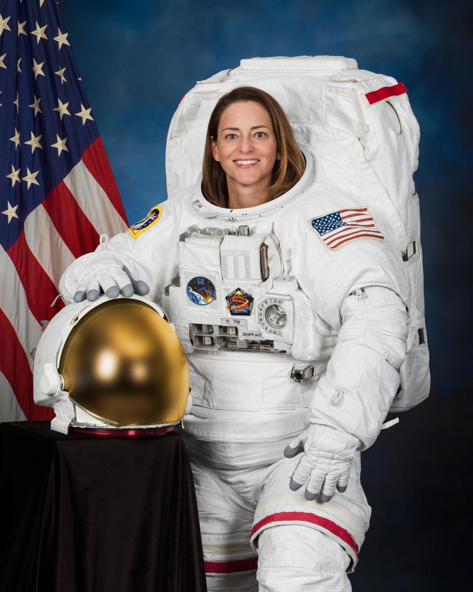 An astronaut in her space suit standing by the American Flag