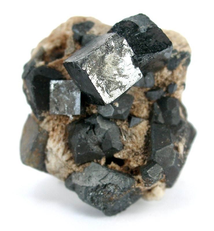 A close-up image of a pyrite mineral cluster. The pyrite crystals are metallic and have a cubic structure, contrasting sharply with the surrounding darker, rougher rock matrix. The crystals capture light, giving them a shiny, reflective appearance.