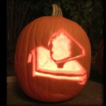 View of an illuminated jack-o'-lantern style pumpkin carved with an image of overview of the James Webb Space Telescope with its distinctive sunshield and mirror components.