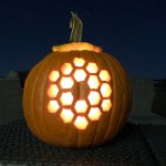 View of an illuminated jack-o'-lantern style pumpkin carved with an image of the 18 hexagon mirror segments of the James Webb Space Telescope.