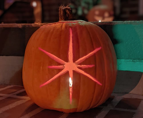 View of an illuminated jack-o'-lantern style pumpkin carved with an image of an 8 pointed star.