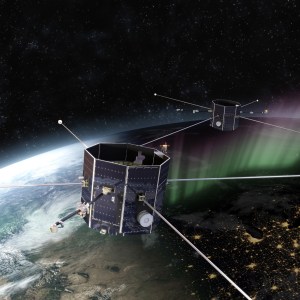 In this artist's concept, the two TRACERS spacecraft are orbiting above Earth. Earth fills most of the image, with speckles of a starry sky visible above the planet. The spacecraft are octagonal with long antennae sticking out on four sides, and shorter antennae sticking out on two sides.