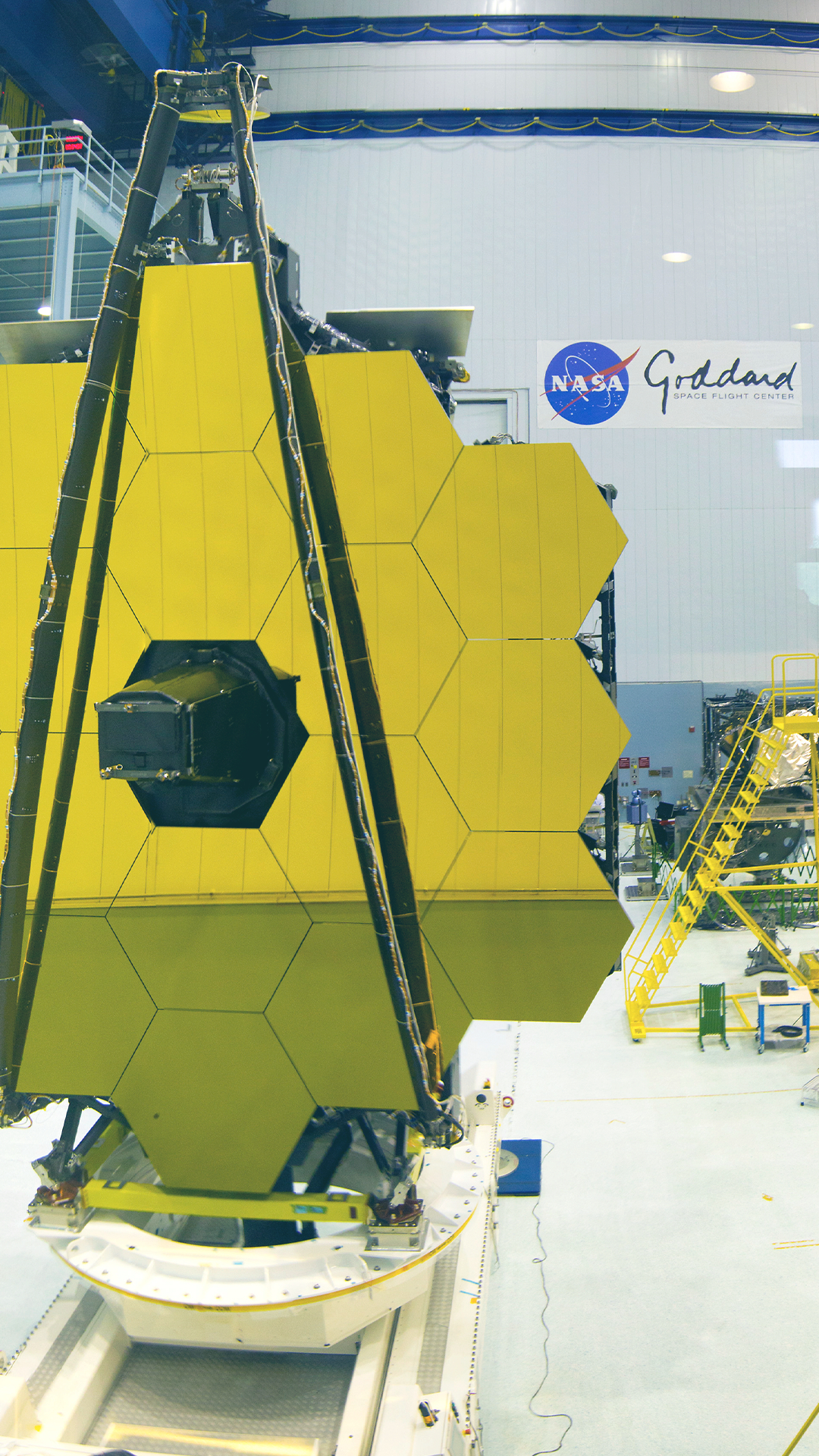 Vertical blurred view of the Goddard Clean Room with the Webb Primary Mirror on test stand in left side foreground with other clean room structures in the background.