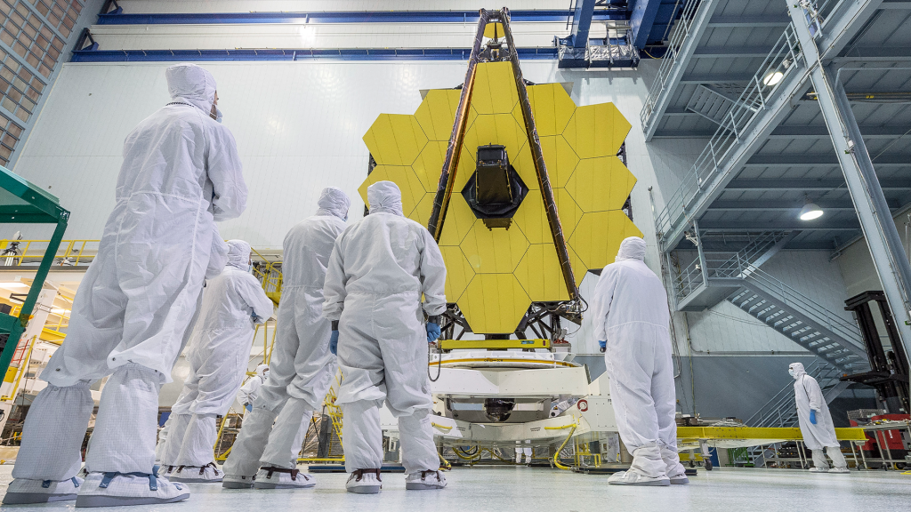 Ground-level view of Webb Primary Mirror with technicians in foreground in the Goddard Clean Room.