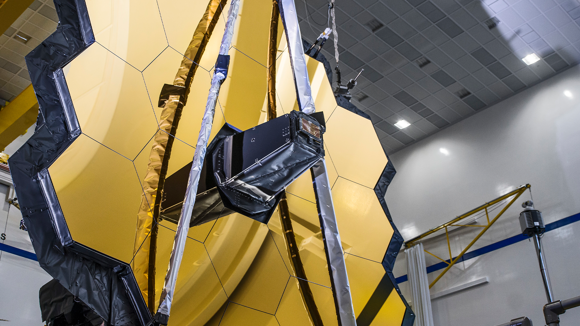 Super closeup view of Webb Primary Mirror in the left side foreground and some clean room structures in the right side background.