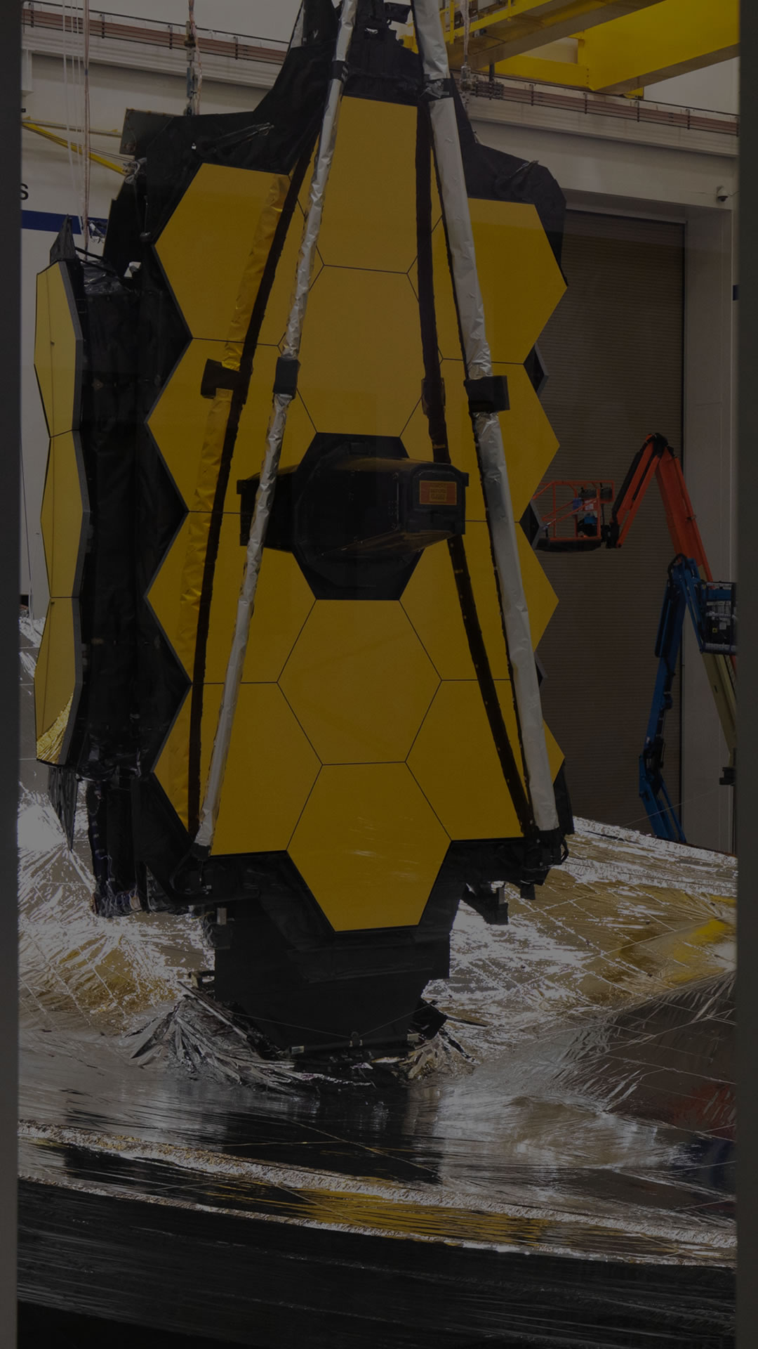 Vertical darkened view of Webb with sunshield and mirrors with two mirror wings folded in the Northrop Grumman Clean Room.