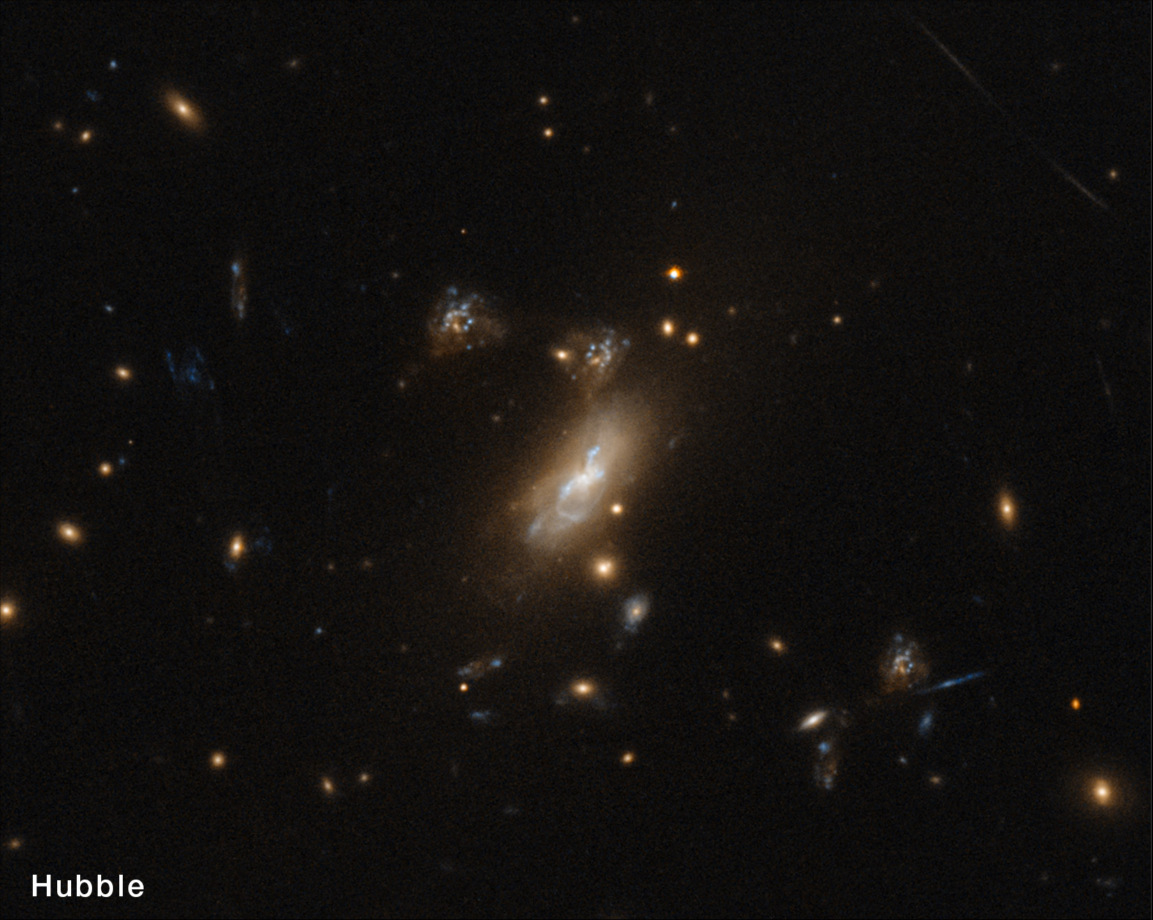 Hubble View: The same region of space in side-by-side images. The left image is labeled “Hubble” and the galaxies shown have an overall yellow tone and haze. The image on the right is labeled “Webb.” In the center of that image, several images of an elongated red galaxy for a shape like the top of a question mark. In comparison it’s clear that some of the features creating the question mark shape are present in the left-hand image as well, but probably wouldn’t be noticed if that image stood alone. The right-hand image is more colorful and defined than the image on the left, with shades of white, red, and a little blue.