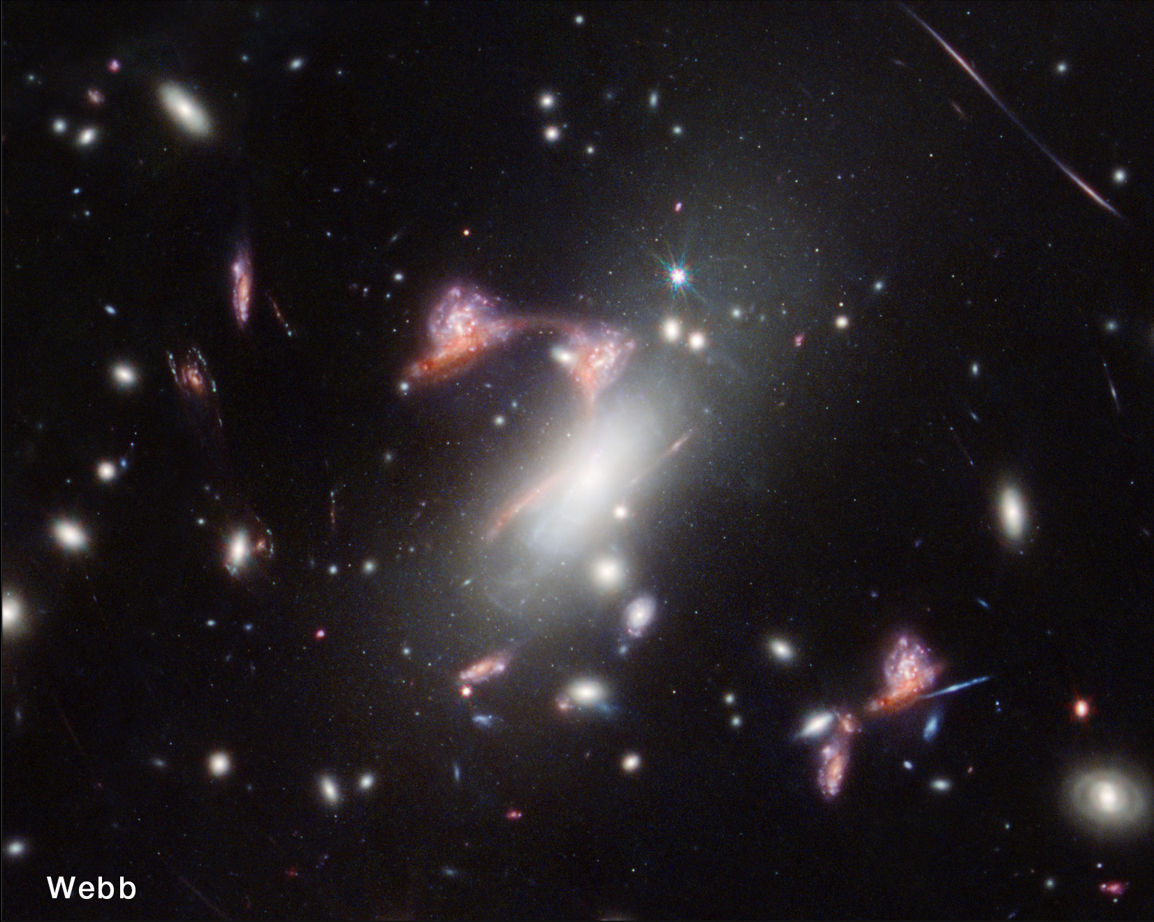 Webb View: The same region of space in side-by-side images. The left image is labeled “Hubble” and the galaxies shown have an overall yellow tone and haze. The image on the right is labeled “Webb.” In the center of that image, several images of an elongated red galaxy for a shape like the top of a question mark. In comparison it’s clear that some of the features creating the question mark shape are present in the left-hand image as well, but probably wouldn’t be noticed if that image stood alone. The right-hand image is more colorful and defined than the image on the left, with shades of white, red, and a little blue.