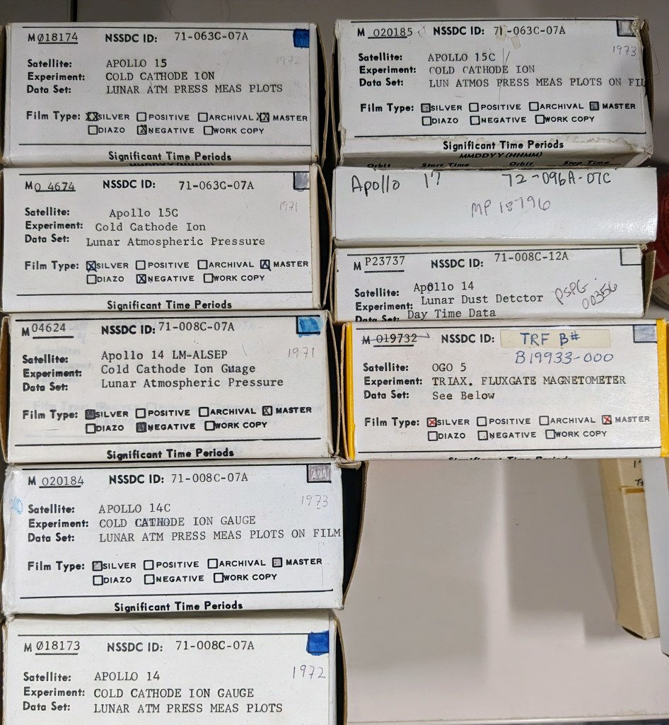 Three side-by-side images. First Image: A collection of rectangular boxes stacked in two rows. Each box has a white label with text detailing what’s inside, including experiments and film types. Some labels have handwritten notes and dates. The boxes are neatly arranged on a shelf. Second Image: A hand holding a strip of microfilm up to the light. The strip contains several rows of tiny black-and-white images and text blocks. The top of the strip reads "Mariner IV Pictures of Mars," and some frames are blank, while others show faint images or text. Third Image: A black-and-white image of Jupiter on a screen. The planet's cloudy bands are visible, with a small white spot near the center. A gloved hand points at the image, which is framed by a screen with data and numbers at the bottom.