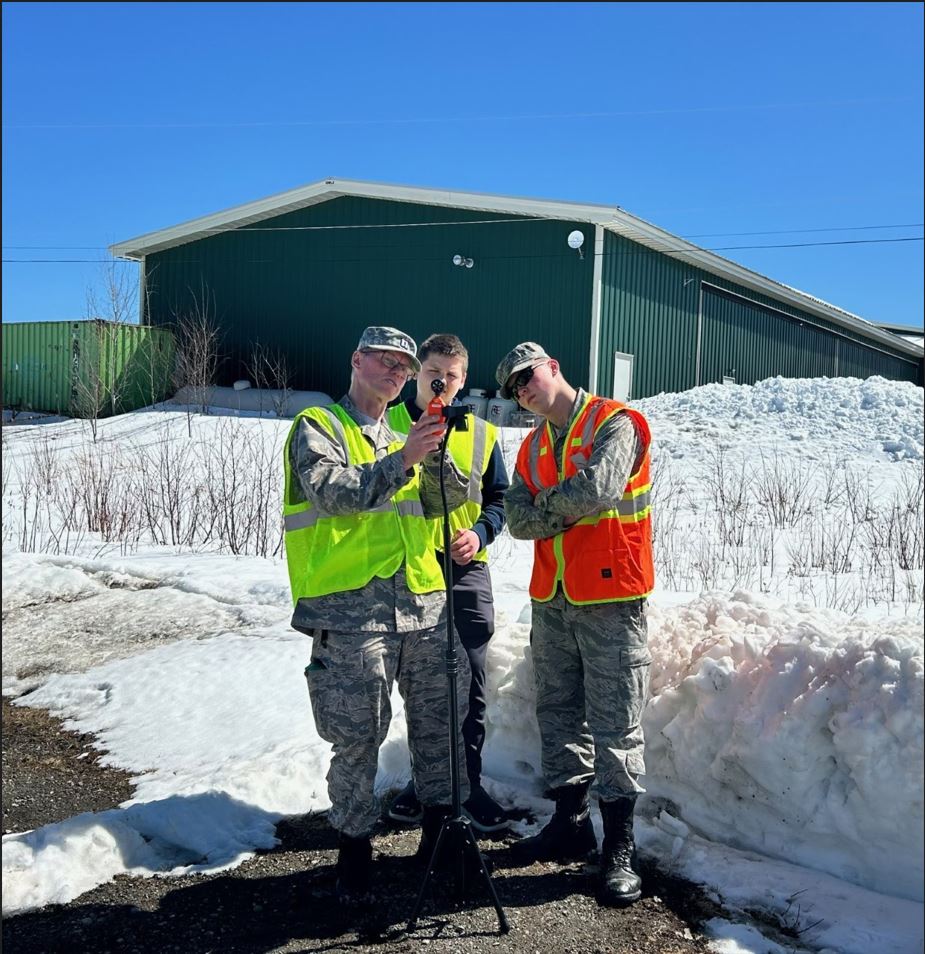 Two male cadets and a senior member collecting wind measurements surrounded by snow.