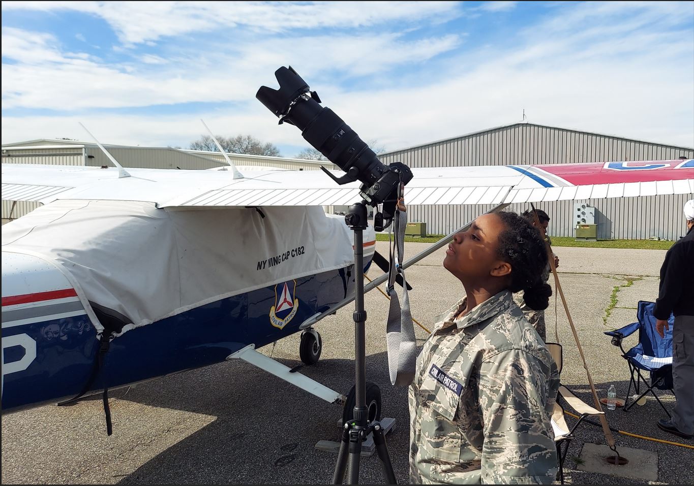 Female cadet looking through a telescope with a solar filter with a Civil Air Patrol Cessna airplane behind her.