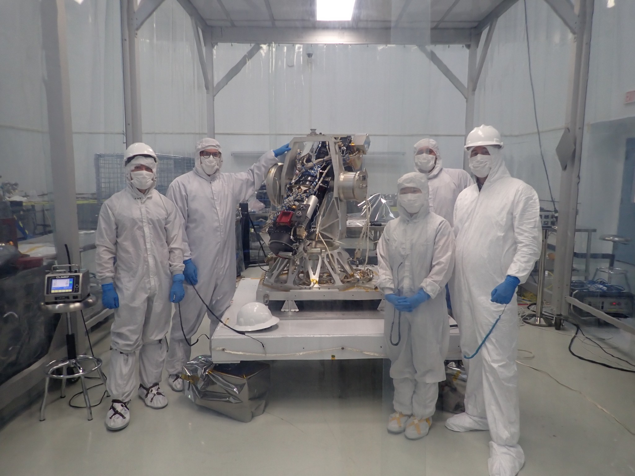 Five people wearing all white suits, helmets, and masks stand by the CODEX instrument.