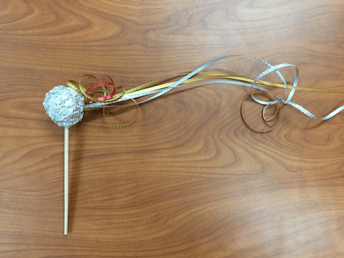 A ball of aluminum foil is attached to a small stick. Ribbons stream out to the right side of the ball.