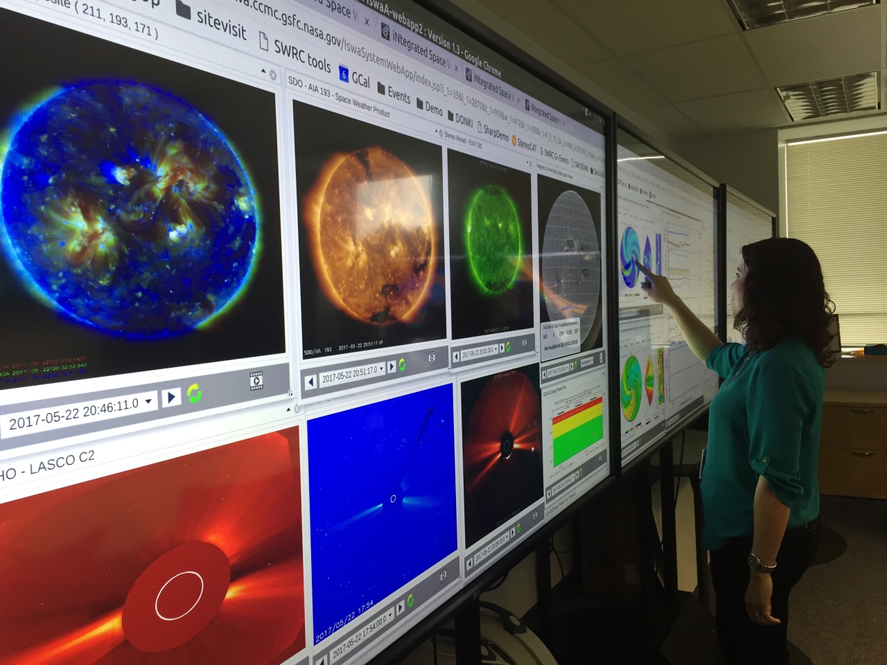 Photo of a woman pointing at a large colorful screen display showing space weather visualiztions.