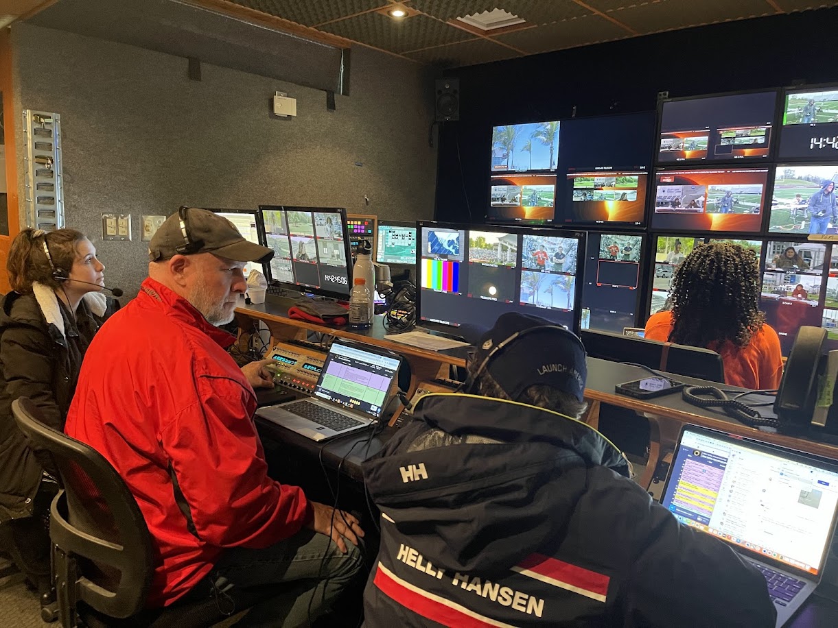 Inside a production truck, multiple people sit in front of computers with large screens showing several views in front of them.