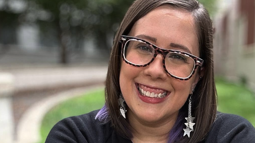 A smiling woman wearing glasses and dangling earrings with stars at the ends of silver chains.