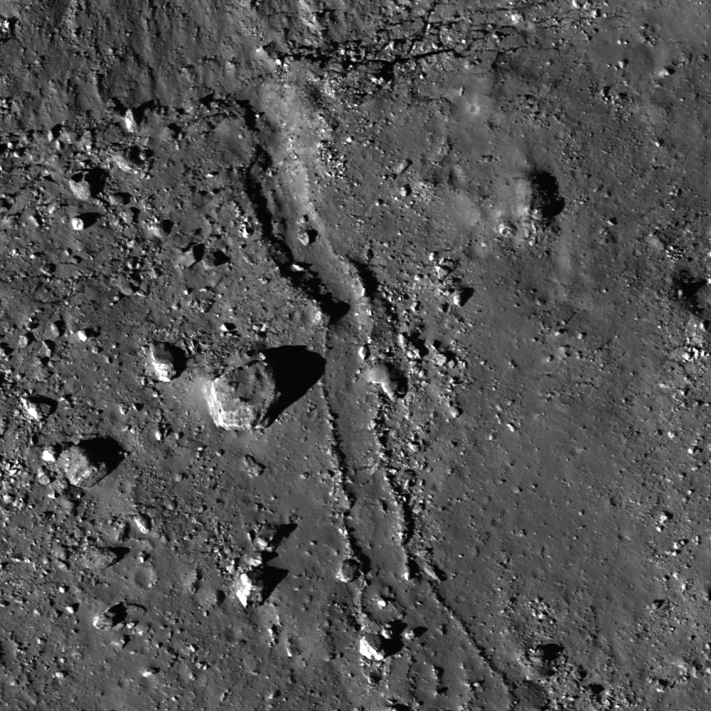 On a gray lunar surface, a feature resembling a groove or channel flows past boulders and rubble.