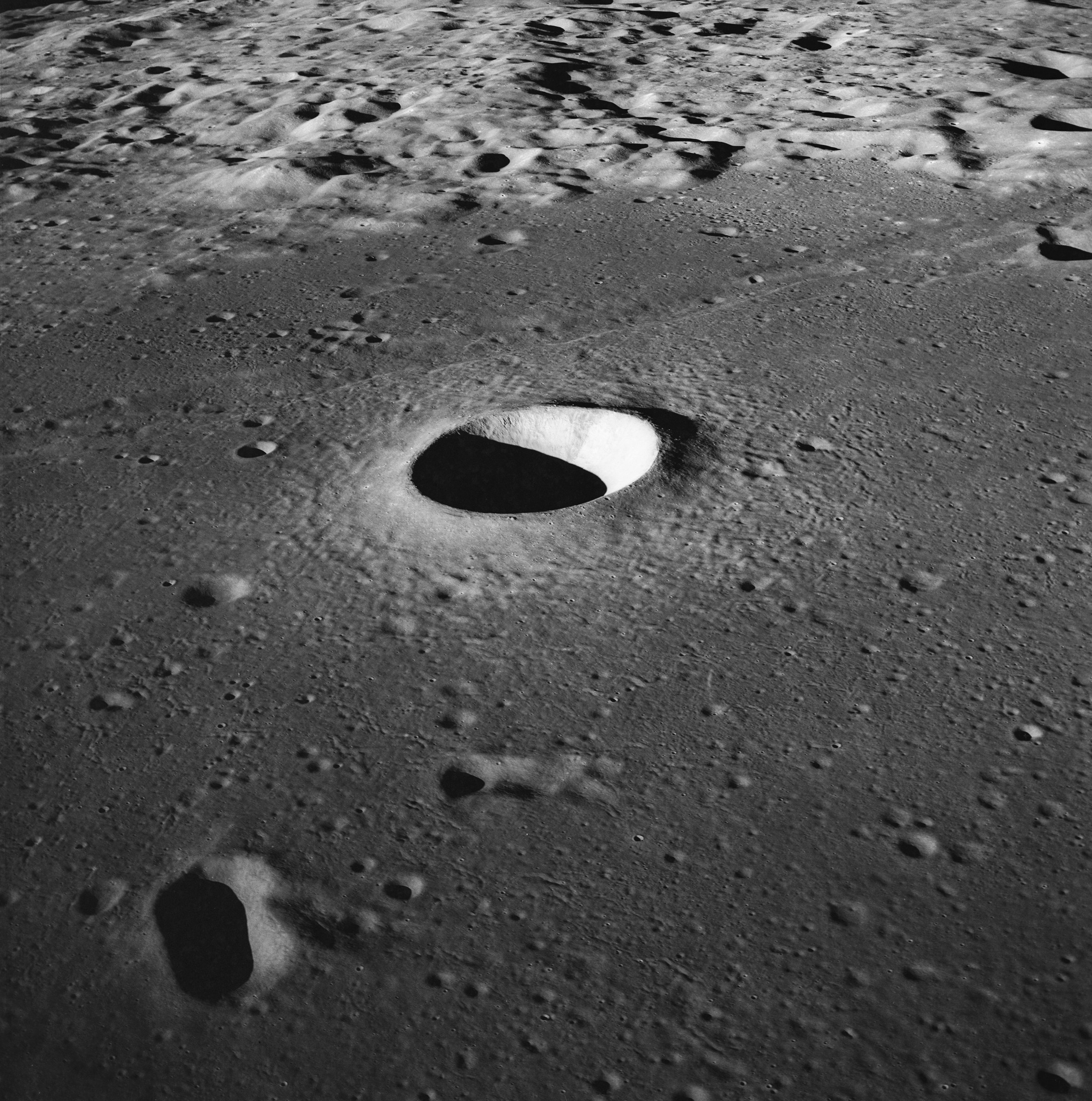 Moltke Crater is a pool of shadow and light on a relatively flat portion of the Moon's surface, surrounded in the distance by more craters and ridges.