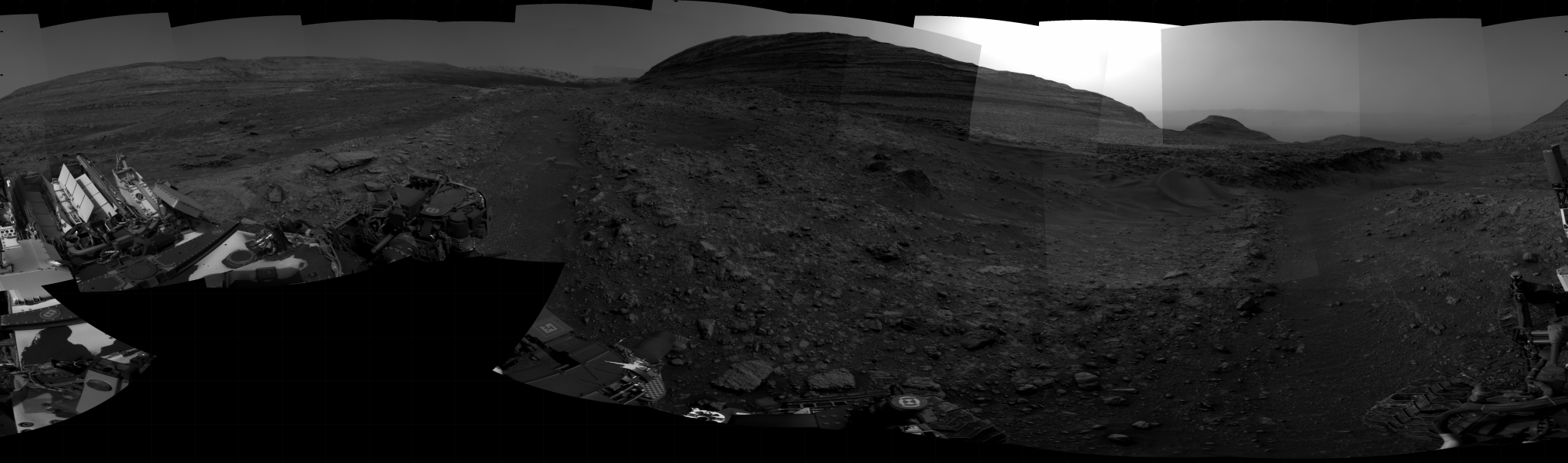 A grayscale panoramic image of the Martian surface shows booth sky and ground with a hill from afar.