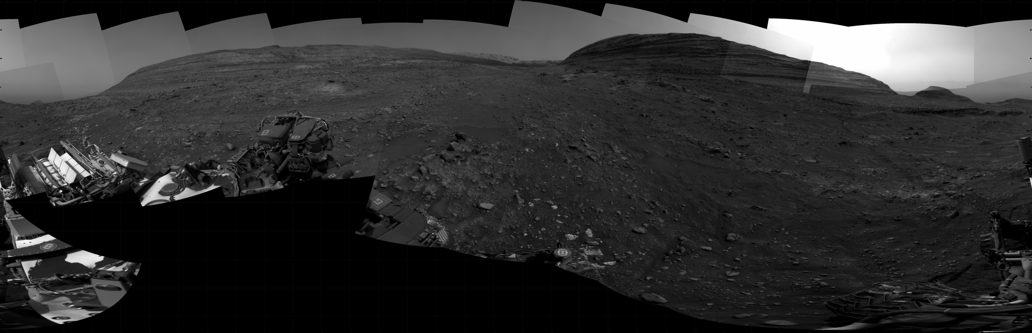 A grayscale panoramic image of the Martian surface shows booth sky and ground with a hill from afar.