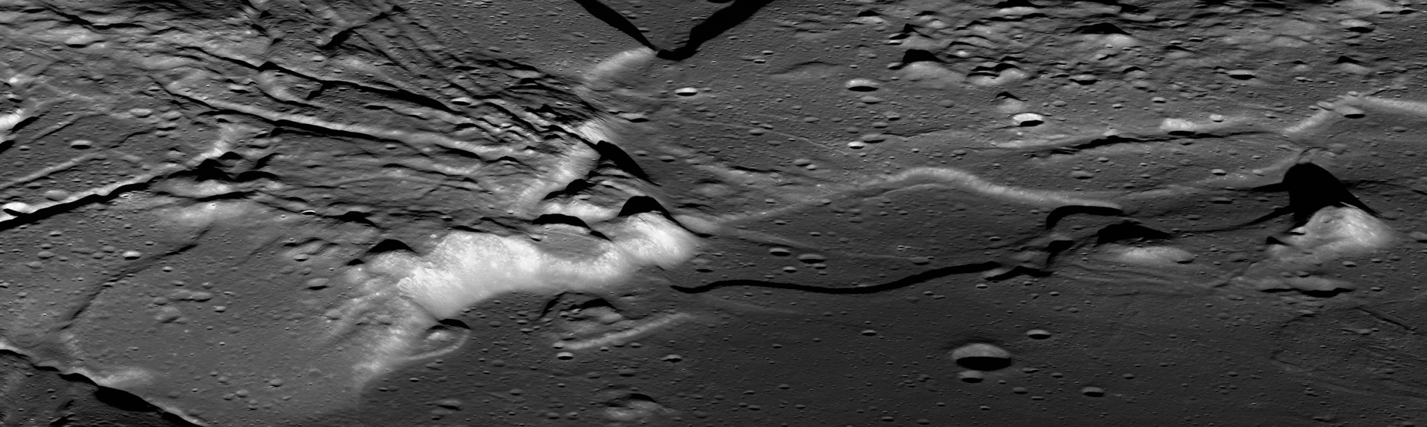 The relatively flat, crater-pocked floor of a basin with mountains to the left. Fissures seem to run away from the peaks, radiating toward the left of the image.